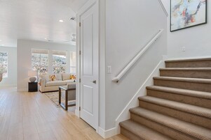A modern interior with a staircase, a living room with a sofa and a view of a mountainous landscape through large windows.
