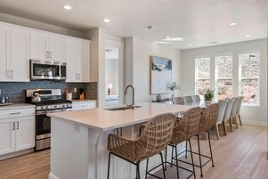 A modern kitchen with white cabinetry, stainless steel appliances, and a large island with wicker bar stools.