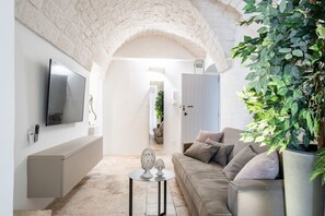 Un salon moderne avec une arche en pierre, un téléviseur à écran plat, un canapé et une petite table agrémentée d’objets décoratifs.