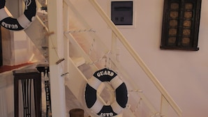 Eine Treppe mit Rettungsringen an den Handläufen, ein kleiner Tisch mit einem Korb und ein gerahmtes Bild an der Wand.