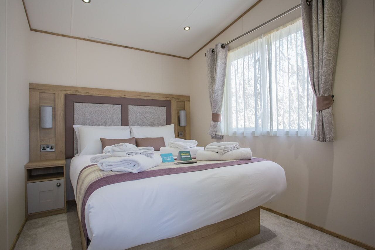 A neatly made bed with towels, a bedside table with a lamp, and a window with curtains.