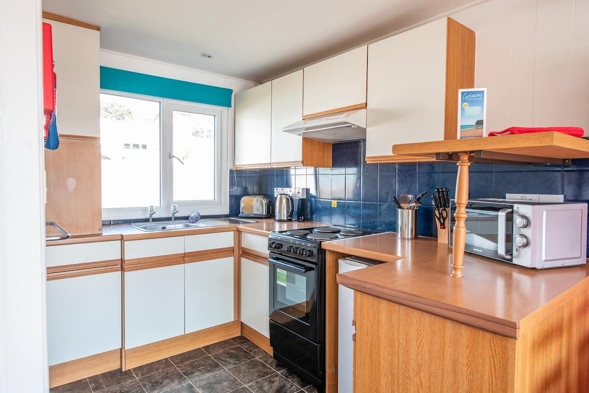 A modern kitchen with white and wooden cabinets, a stove, oven, microwave, and a window with a view.