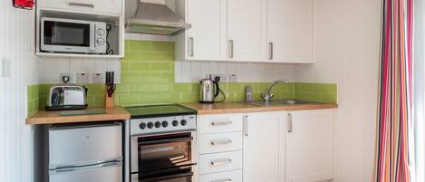 A compact kitchen with white cabinets, a microwave, a stove, and a refrigerator.