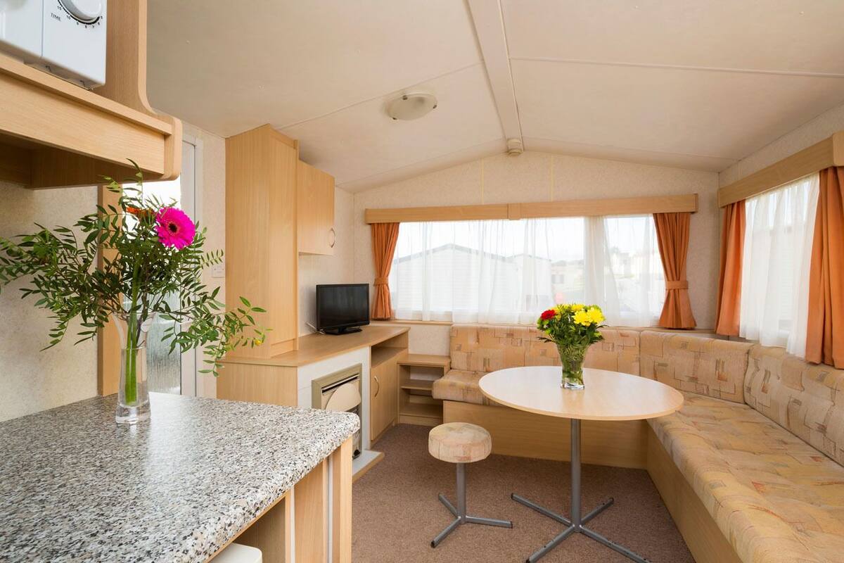 A compact RV interior with a kitchenette, a dining area, and a seating area with a television.