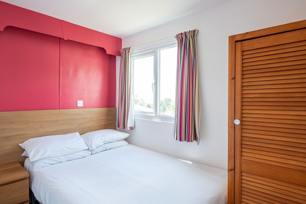 Un dormitorio con cama, cabecera de madera, ventana con cortinas a rayas y armario de madera.