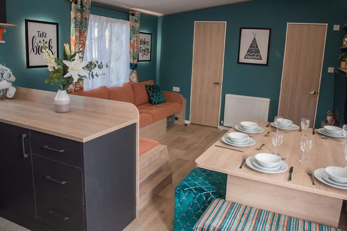 A modern living room with a sofa, a dining table set for four, and a kitchen area with cabinets and a countertop.