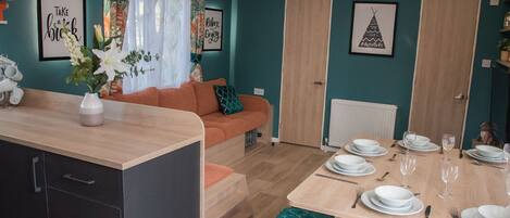 Een moderne woonkamer met een bank, een eettafel voor vier personen en een keuken met kastjes en een aanrecht.