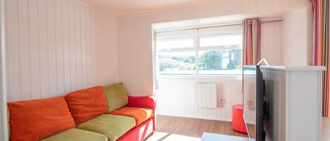 A living room with a red and green sofa, a television, and a window with curtains.