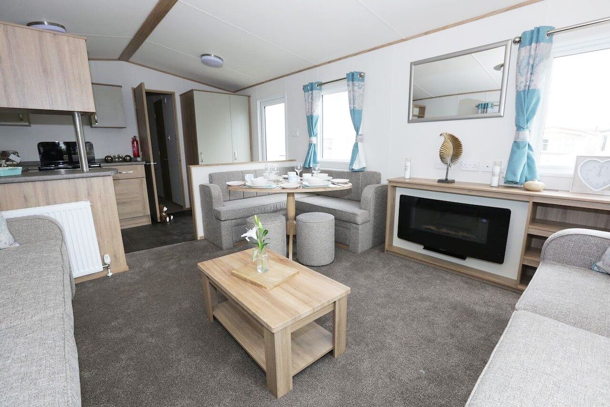 A compact living space with a kitchenette, a seating area with a sofa and a table, a television, and a window with curtains.