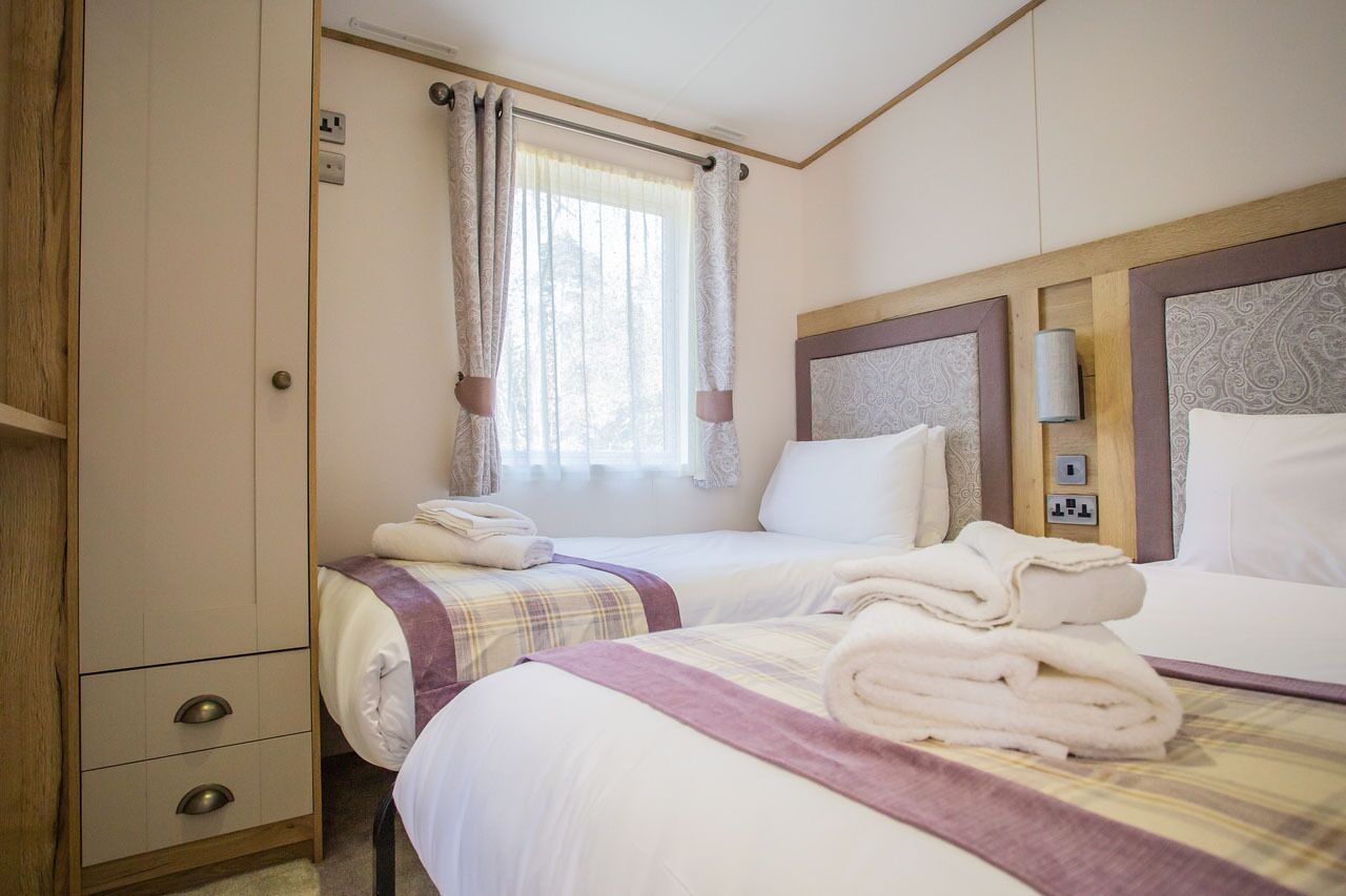 Une chambre d’hôtel avec deux lits, une armoire, une fenêtre avec des rideaux et une lampe fixée au mur.