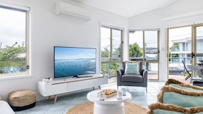 Relax in this stylish living room with a large flat-screen TV, comfortable armchair, and a balcony offering a view of the surrounding neighborhood.