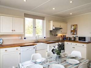 A compact kitchen with white cabinetry, a built-in dishwasher, a microwave, and a dining area with a striped tablecloth.