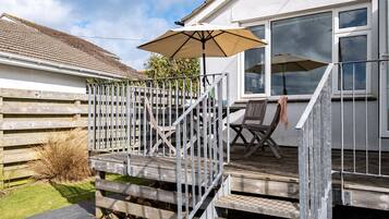 A wooden deck with a metal railing, a beige umbrella, and a chair.
