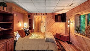 A cozy wooden room with a bed, a dresser, a TV, and a window with blinds. - One of a kind, Creek Front Lodge 3 floors, 2 kitchens, long distance views. (MARS HILL)