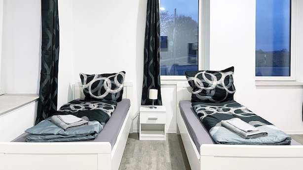 A twin bedroom with two beds, a nightstand, and a window. - Hochwertige Studios für Monteure (Stemshorn)