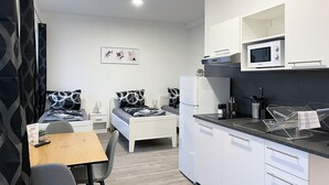 A compact hotel room with a kitchenette, a bed with patterned pillows, a small dining table, and a chair. - Hochwertige Studios für Monteure (Stemshorn)