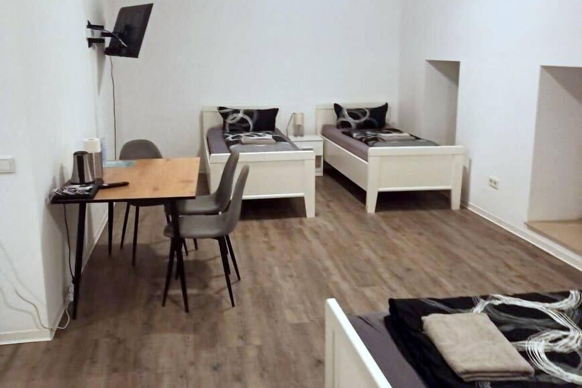 Een kleine, moderne kamer met houten vloer, een bureau met stoel, twee eenpersoonsbedden, een aan de muur bevestigde televisie en een klein tafeltje met lamp.