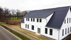 A white building with a dark roof, multiple windows, and a door. - Hochwertige Studios für Monteure (Stemshorn)