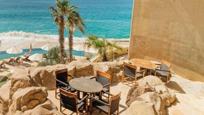 Eine Terrasse mit Meerblick, ausgestattet mit Sitzgelegenheiten und Palmen.