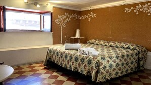 A hotel room with a checkered floor, a bed with patterned bedding, a small table with a lamp, and a window with a view. - Economy Double Room - Interior floor (Catania)