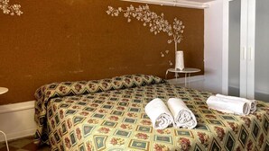 A hotel room with a patterned bedspread, a small round table with a vase, and a wardrobe. - Economy Double Room - Interior floor (Catania)