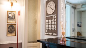 A wall-mounted clock with a calendar below it, a framed picture, and a red sign on the wall.