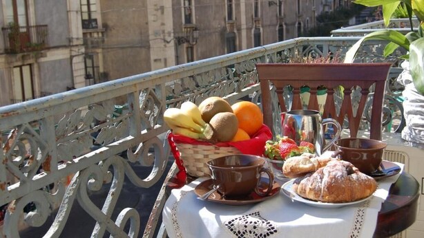 A balcony with a table set for breakfast, including fruits, pastries, and a coffee cup. - Double or Twin Room (Catania)