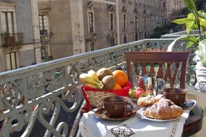 Un balcón con una mesa dispuesta para el desayuno, que incluye frutas, pasteles y una taza de café.