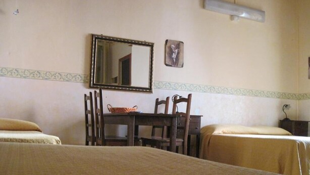 A hotel room with two beds, a wooden table with chairs, a mirror, and a small decorative item on the wall. - Family room (Catania)