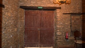 A stone-walled room with a wooden double door labeled "SORTIDA," a chandelier, a fire extinguisher, and a chair.