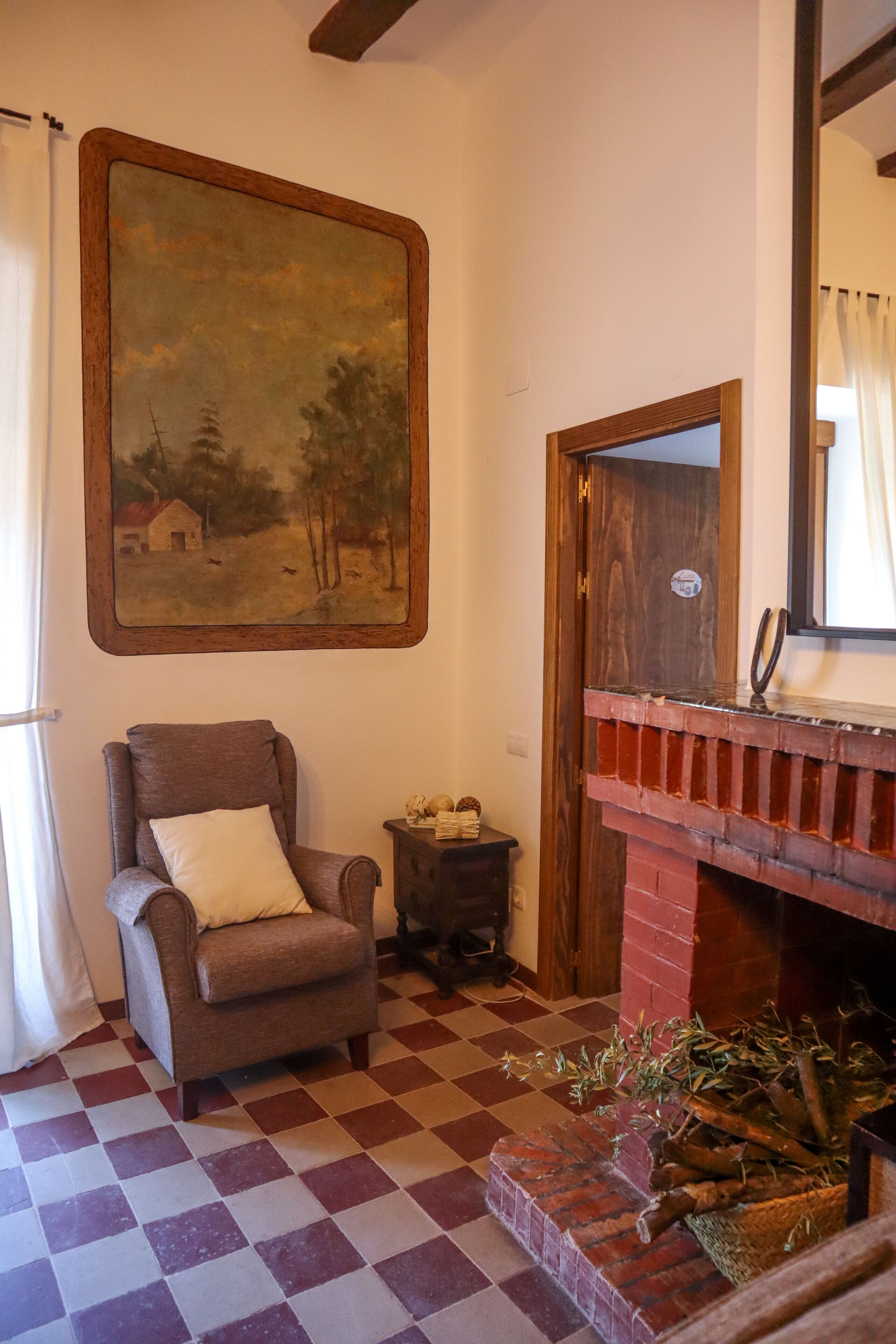 Ein Zimmer mit Schachbrettmuster-Boden, einem Gemälde in Holzrahmen, einem Kamin aus Ziegelsteinen und einer Holztür.