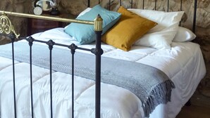 A bed with a stone wall background, a metal headboard, and a bedside table with a clock.