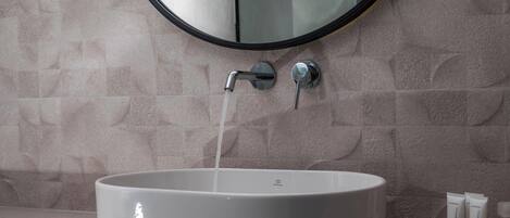 A bathroom with a round mirror, a sink with running water, and toiletries on the counter.