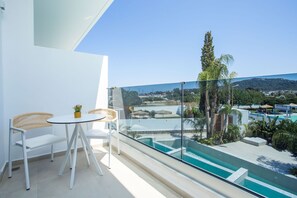 A balcony with a glass railing, a pool, and a view of a town. - Vanik Suites (Rhodes)