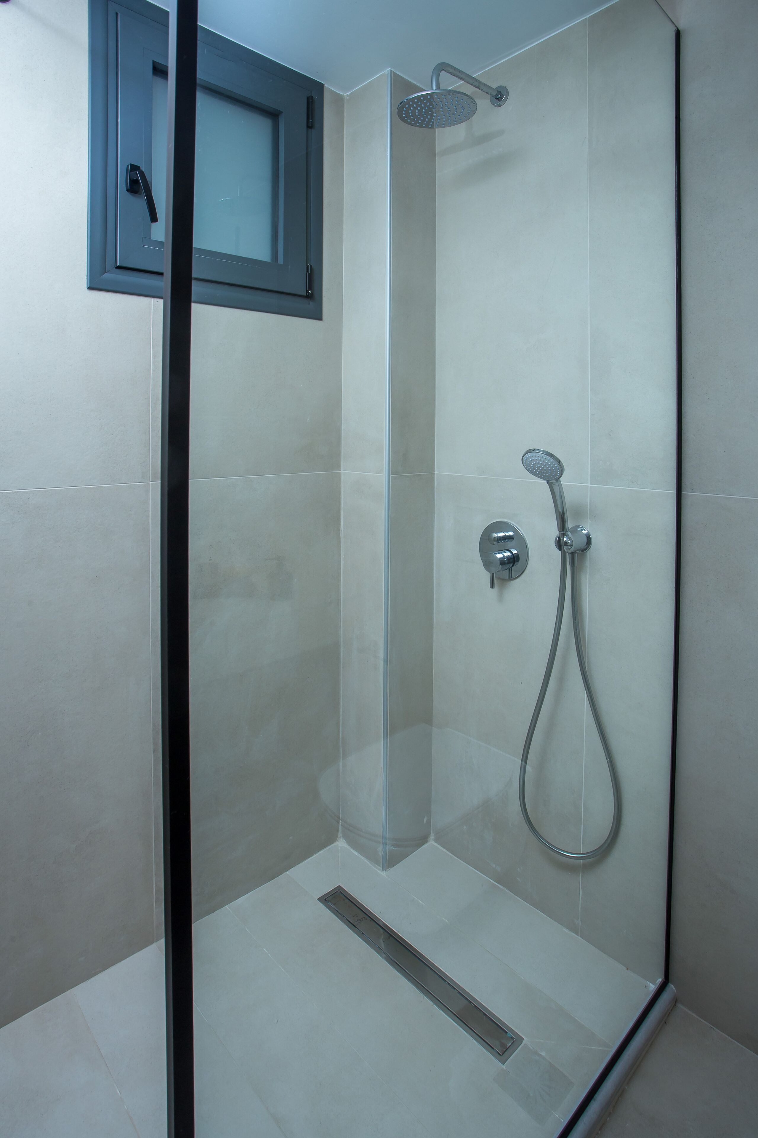 A glass-enclosed shower with a handheld showerhead and a wall-mounted control.