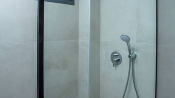 A glass-enclosed shower with a handheld showerhead and a wall-mounted control.