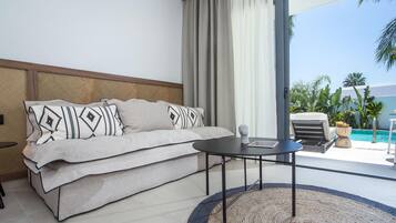 Habitación de hotel moderna con sofá, una mesita y vistas a una piscina y palmeras.