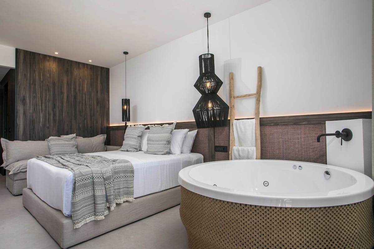 Un dormitorio moderno con una cama grande, una bañera independiente y una lámpara colgante original.