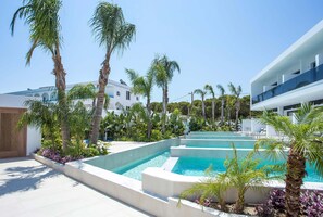 A modern pool area with multiple levels of infinity pools, surrounded by palm trees and a white building with balconies. - Vanik Suites (Rhodes)
