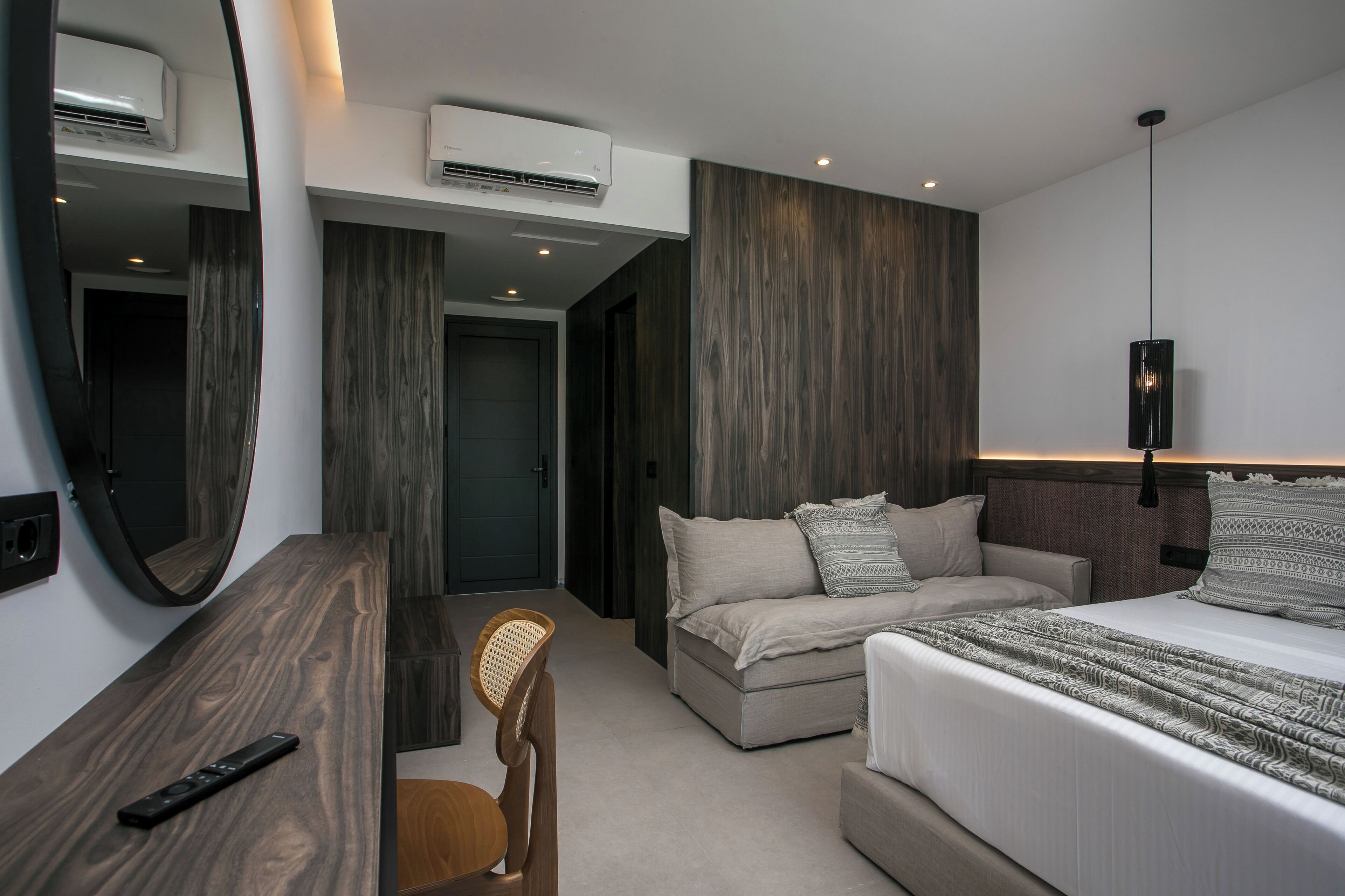 A modern hotel room with a large bed, a desk, a chair, and a mirror.
