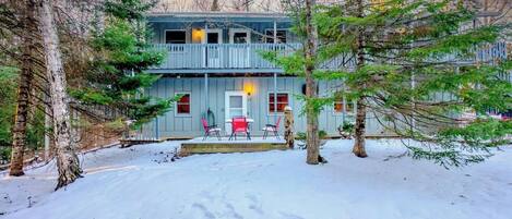 A two-story cabin with a covered porch and a snow-covered yard.