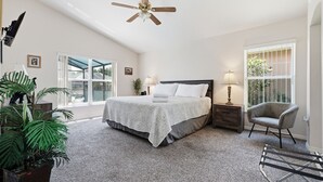 Een slaapkamer met een bed, bedlampen, een plafondventilator, een stoel en een groot raam.