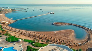 An aerial view of a coastal resort with a curved beach, a long pier, and a pool area. - SUNRISE Alma Bay Resort (Hurghada)