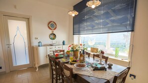 A dining area with a table set for four, a window with blinds, and a view of the outdoors. - Villa Olimpia 6 2 in Castellammare del Golfo (Castellammare del Golfo)