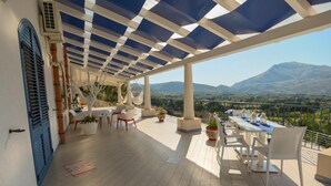 A covered outdoor terrace with a view of mountains, furnished with white chairs and tables, and decorated with potted plants. - Villa Olimpia 6 2 in Castellammare del Golfo (Castellammare del Golfo)