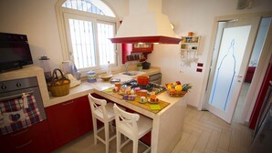 A kitchen with a gas stove, a sink, and a window. There are two white chairs, a red cabinet, and a microwave. - Villa Olimpia 6 2 in Castellammare del Golfo (Castellammare del Golfo)