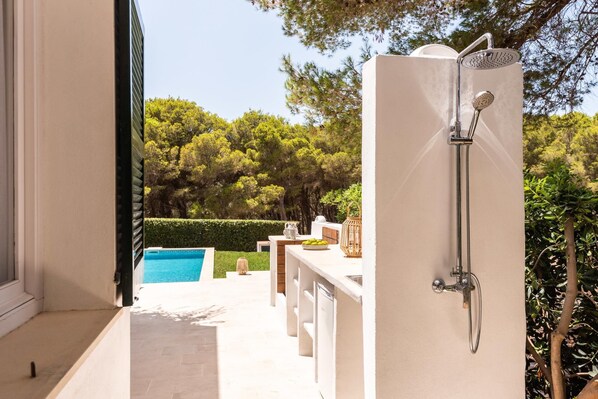 A modern outdoor shower area with a pool in the background.