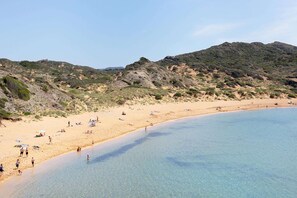 A beach with clear water, sandy shore, and hills in the background.