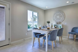 A dining area with a white table, grey upholstered chairs, and a decorative wall piece.