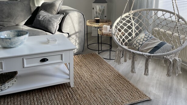 Un salon moderne avec un canapé gris, une table basse blanche et un fauteuil suspendu orné d’un motif en macramé.